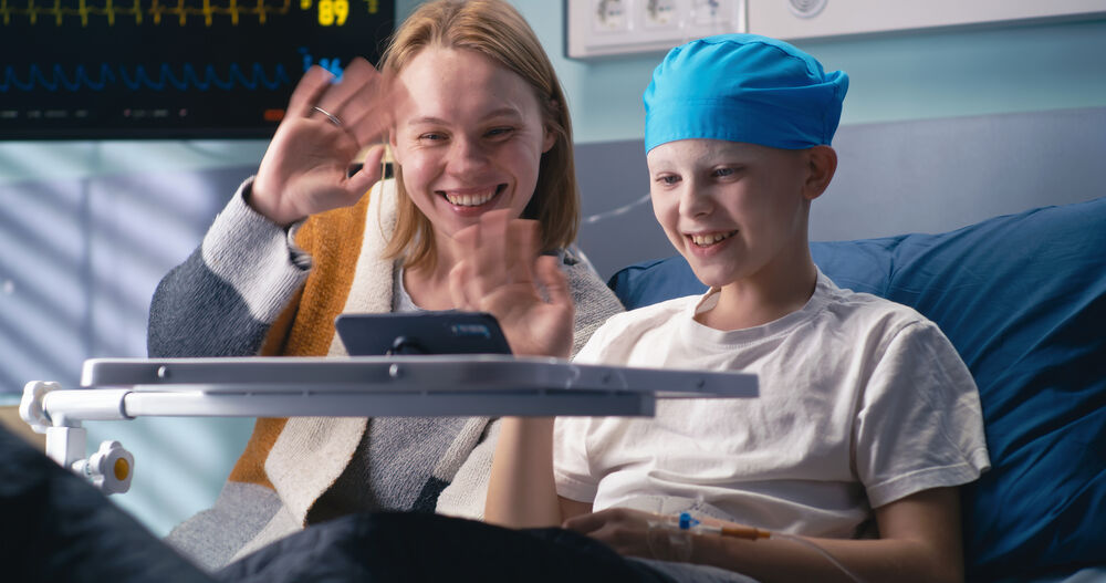 Child and parent in oncology ward waving to someone on a mobile video call