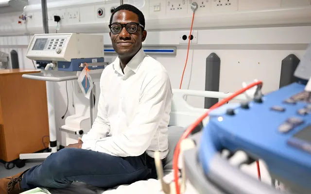 Researcher Dr Wezi Sendama sat on a clinical bed surrounded by medical equipment