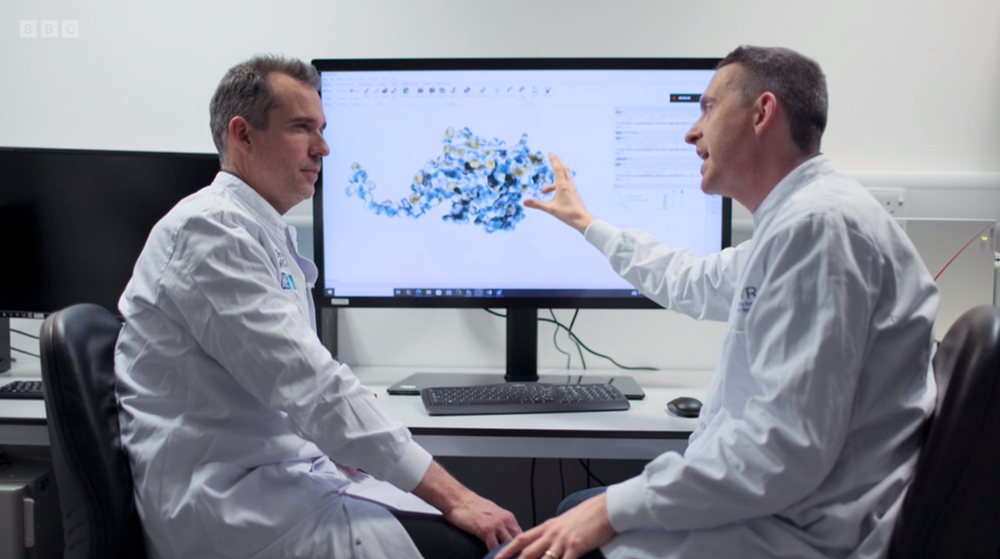 Screenshot from BBC documentary where Dr Joe Grove discusses his research with Dr Chris van Tulleken, sitting in front of computer screen.