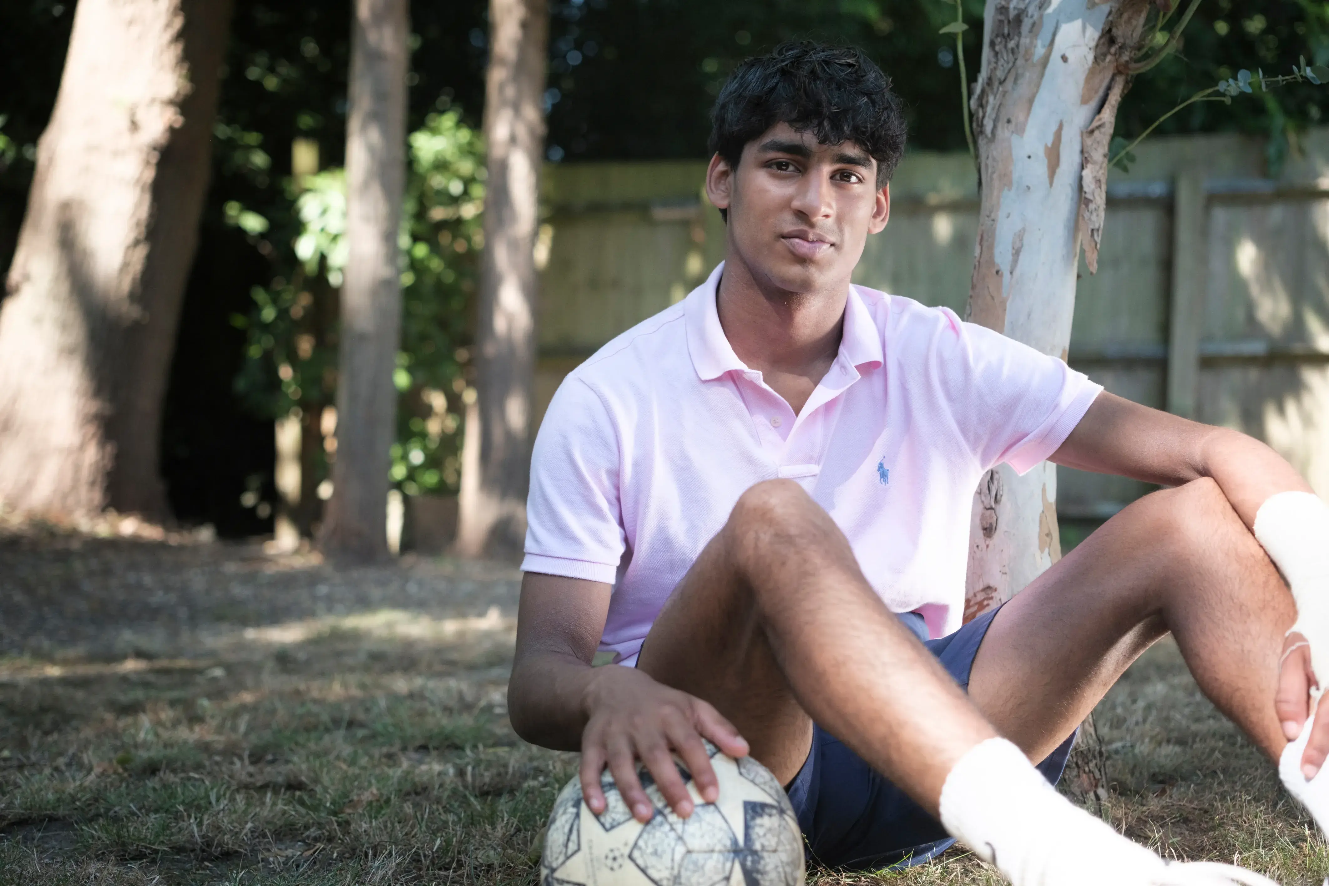 Akshay, a young man, sits with a football in the garden