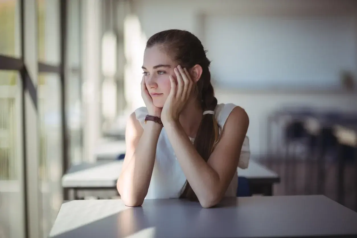 Thoughtful schoolgirl sitting in classroom 660249744 1258x838