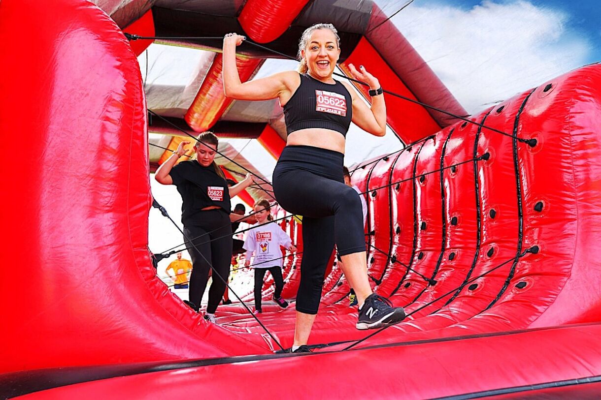 White female runner on a red inflatable smiling at camera with arms in the air