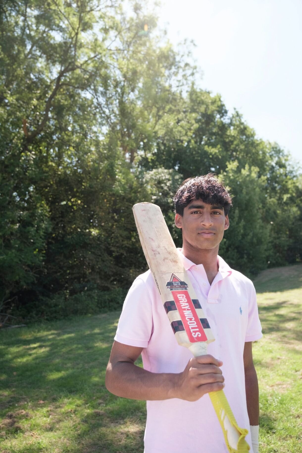 Akshay stands with cricket bat on shoulder in park