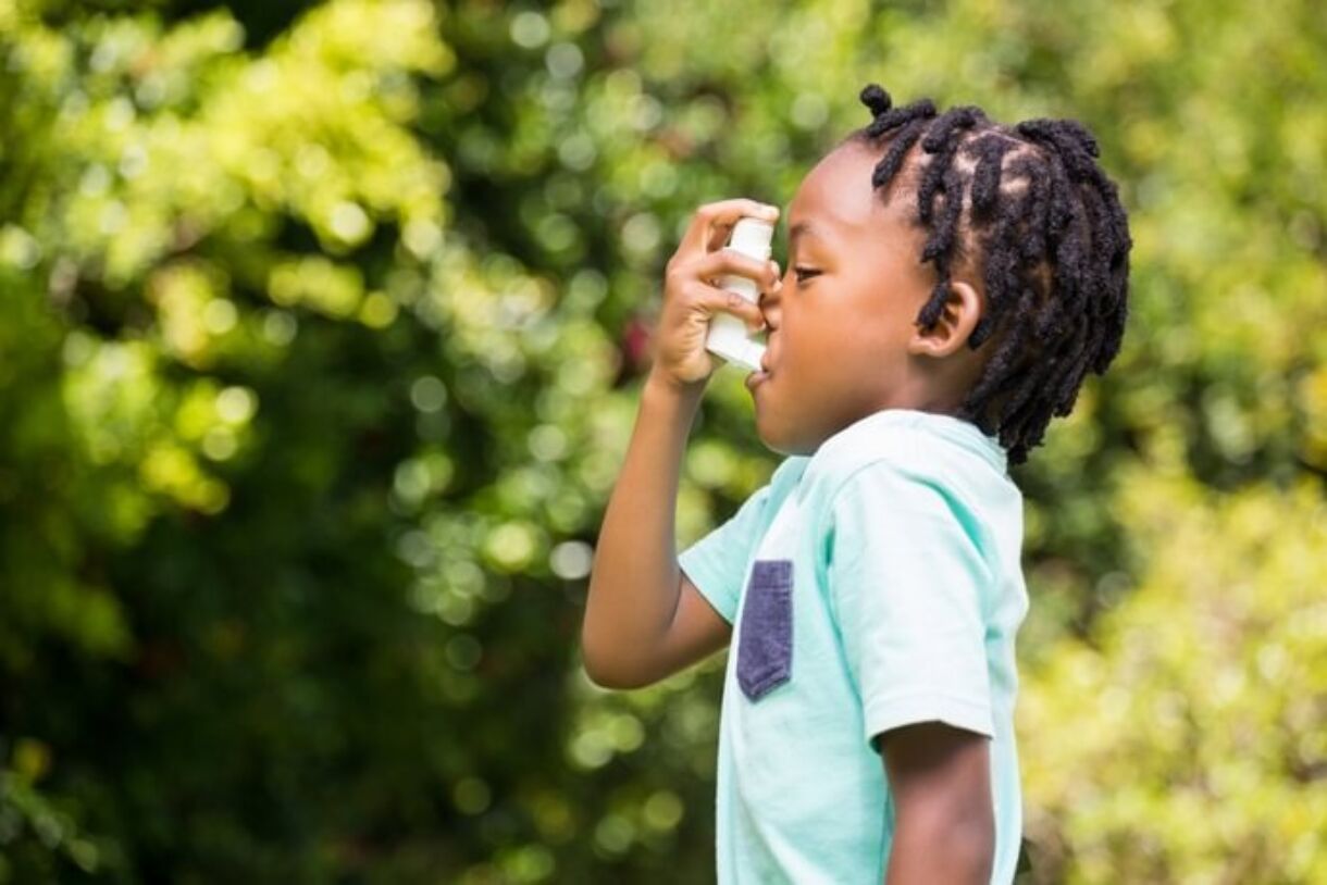 Young child outdoors using an asthma inhaler