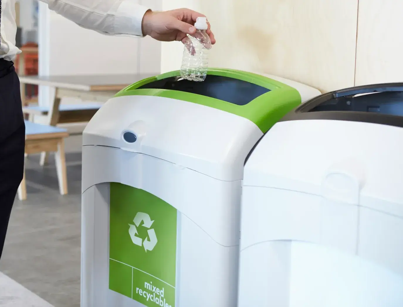 Person dropping a plastic bottle into an office recycling bin