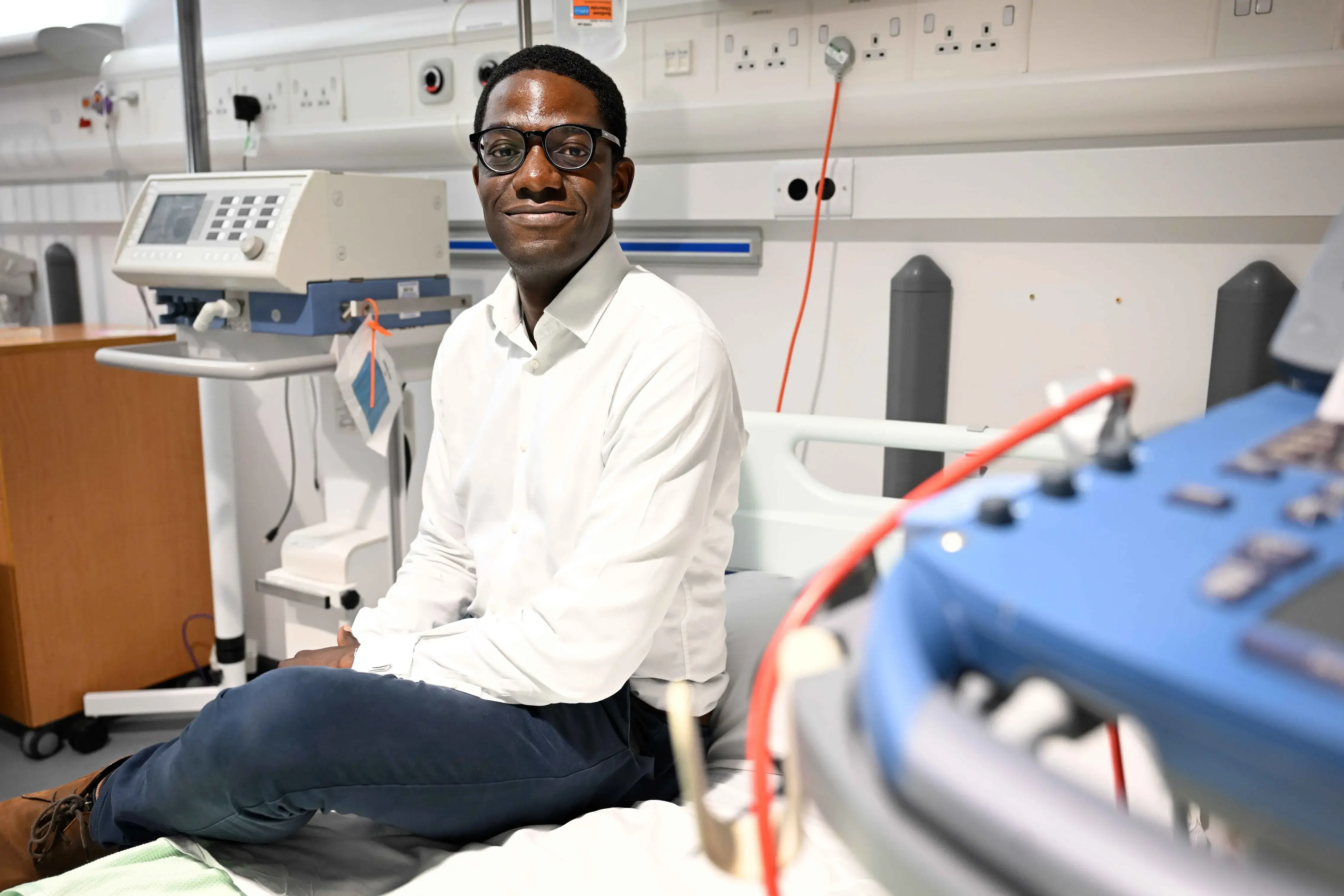 Wezi sits on a bed amongst medical equipment